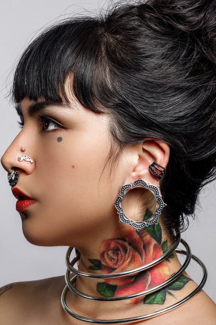 Woman with tattoos and piercings wearing large gauge eyelets against a gray background